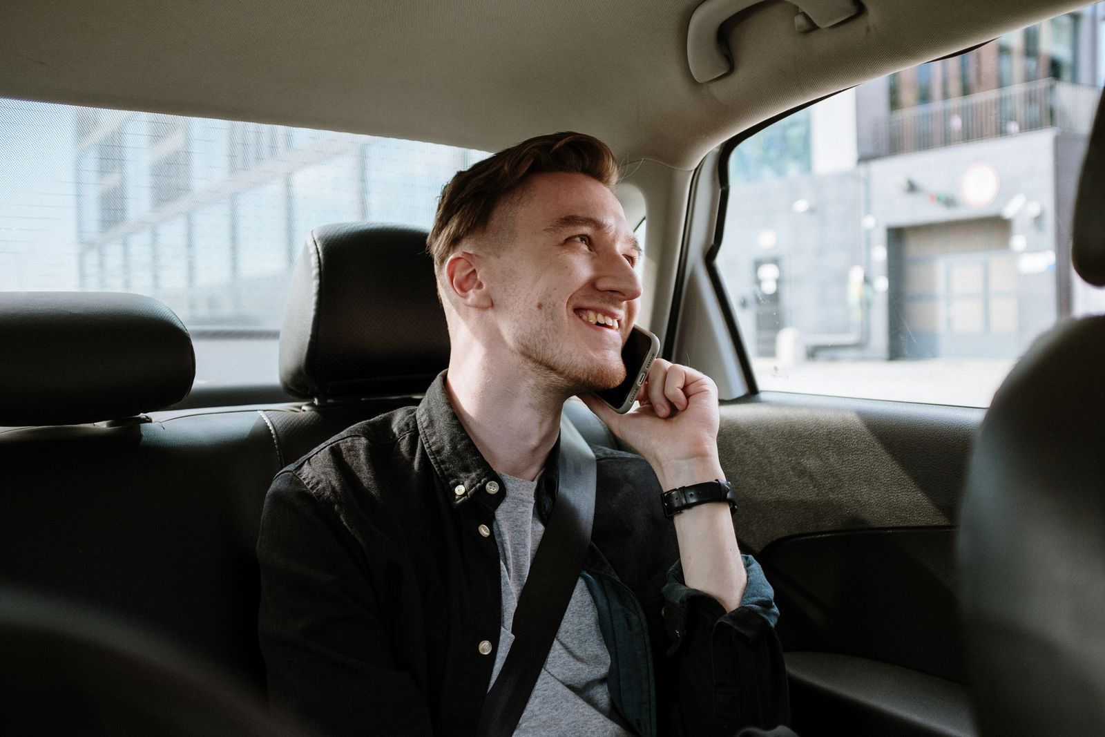 A man in the back of a car mid-call, phone held to his ear
