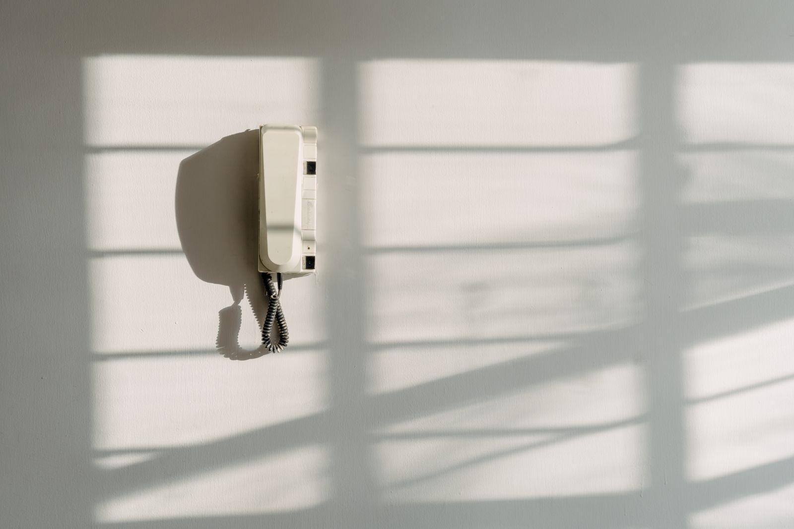 A wall-mounted phone with the handset on its hook in an empty, sunlit room