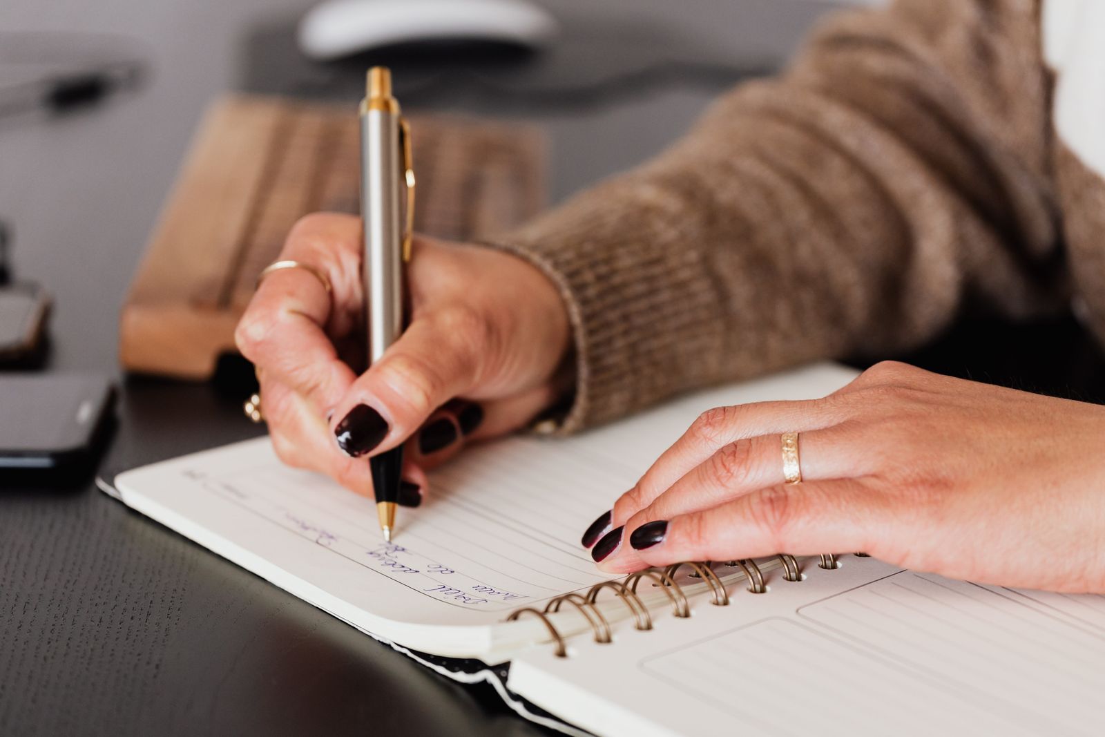 Hands writing an appointment into an open desk diary