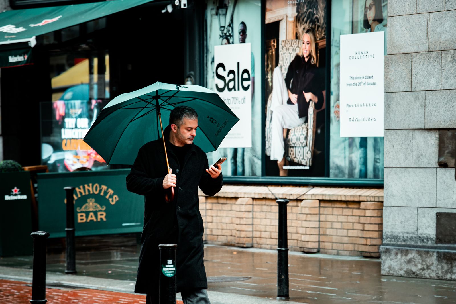 A negotiator checking his phone under an umbrella on a rainy street