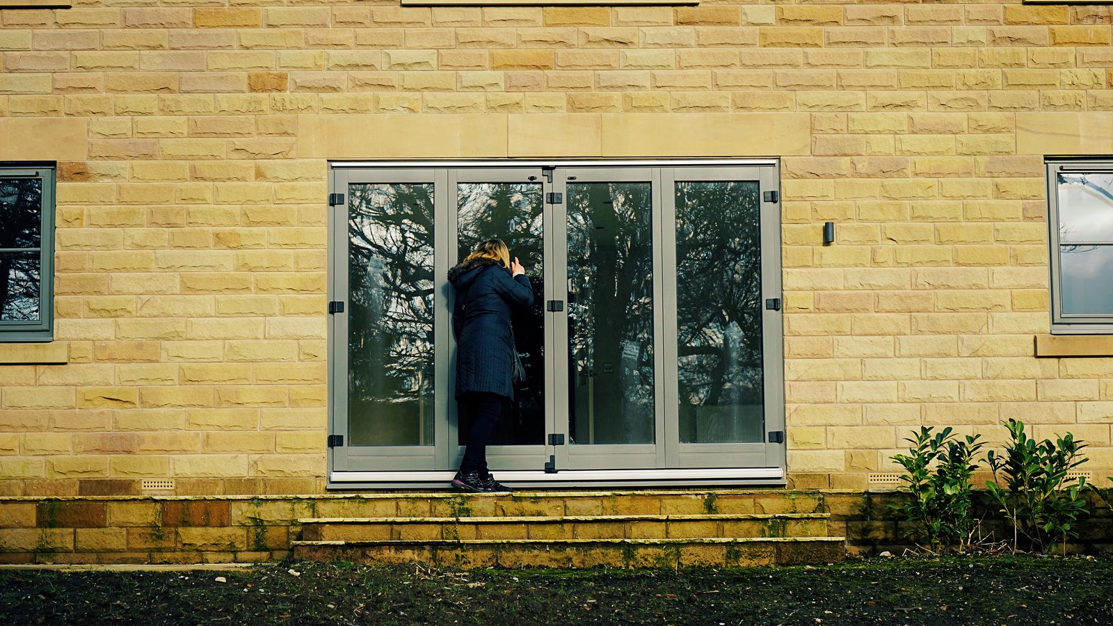 A woman peering through the glass doors of a Yorkshire stone house
