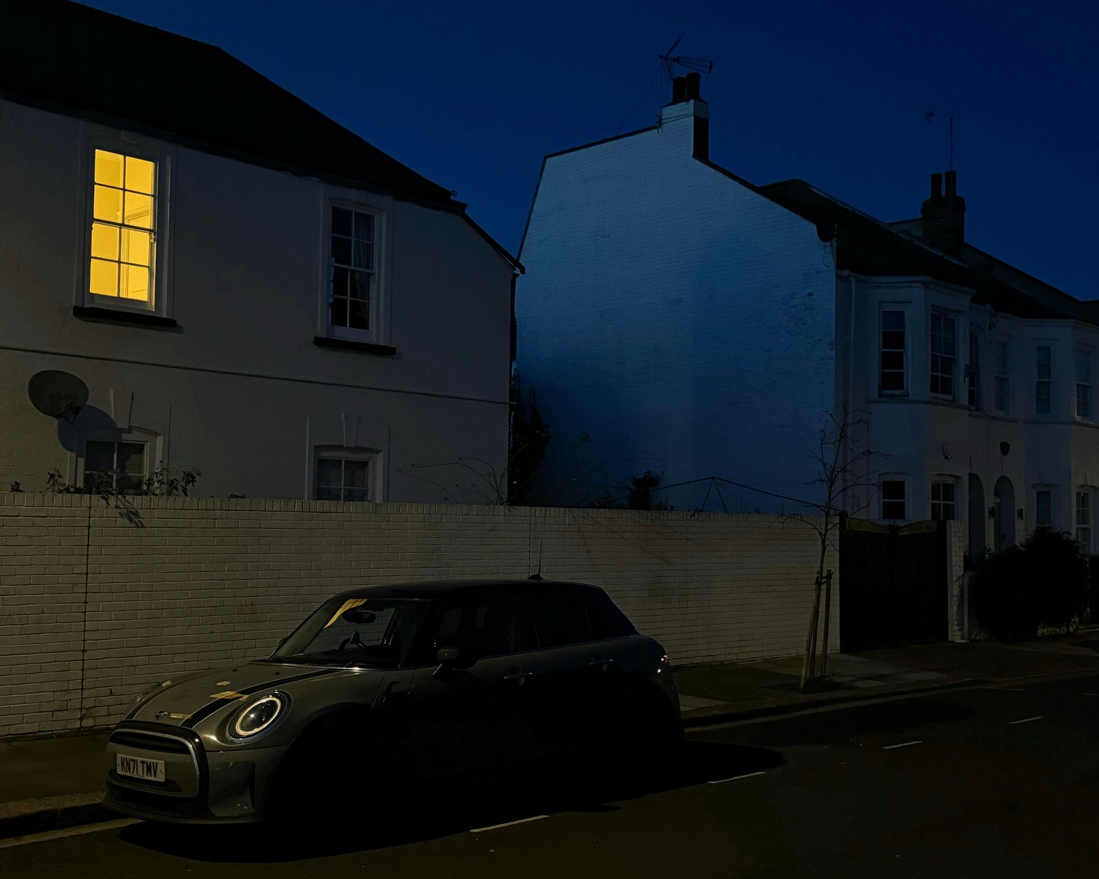 A dark residential street at night with a single lit window